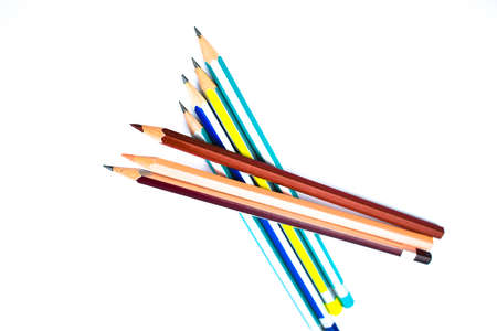 Seven different colored wood pencil crayons arranged on top of each other on a white background