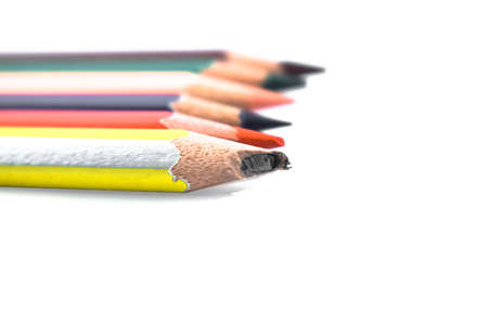 Some different colored wood pencil crayons placed in a line behind one another on a white background