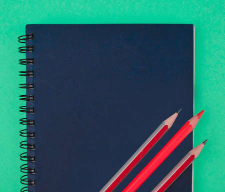 Three red colored wood pencil crayons placed on top of a blue color paper diaryの写真素材