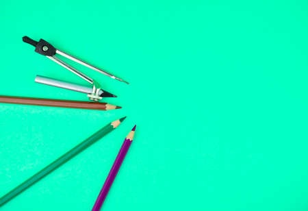 Compass and three different color wood pencil crayons placed on top of a light blue paper background