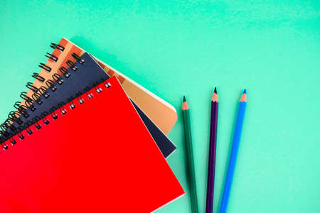 Three different colored note paper diary and pencil crayon placed beside each other on a blue paper backgroundの写真素材