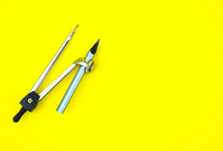 One compass attached to a silver color wood pencil crayon on a yellow paper background