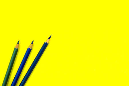 Three dark blue colored wood pencil crayon placed on top of a yellow paper backgroundの写真素材