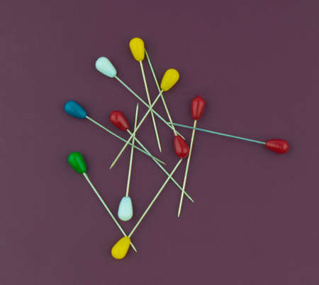 Some different colored brooches pin placed on top of a purple color paper background
