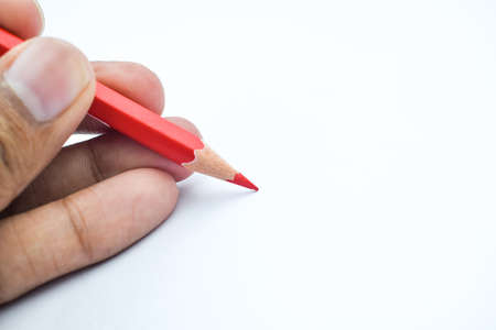 A man writing with a red pencil crayon with a sharp tip on a white paper backgroundの写真素材