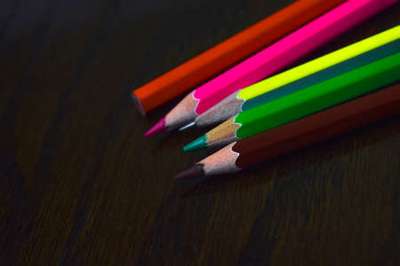 Five different colored wood pencil crayons placed on top of one another on a desk
