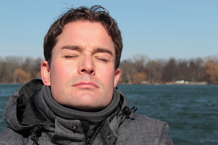 Man relaxing on a lakesite facing the sun eyes closed