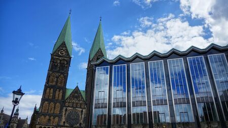 Bremen, Germany. Parliament of Bremen German: Bremische B rgerschaft and towers of the Bremen Cathedral (German: 'Bremer Dom') on a sunny day. Partly cloudy sky mirrored in the huge glass front of the government building.の写真素材