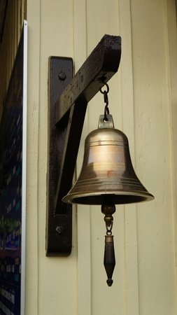 Bronze Bell hanging on wooden dark hook at bright wooden wall. Photo taken at a train station in...
