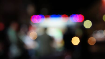 Blurred unfocused scene with people ordering food in front of an illuminated food booth. Red blue...