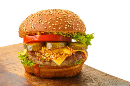 Classic burger with beef, cheese vegetables in sauce on a bun with sesame seeds on a wooden board on a white background.の写真素材
