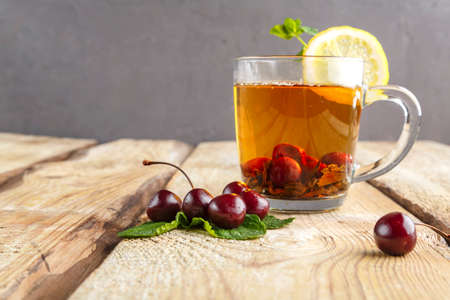 black tea in a glass cup with mint cherries and lemon on a wooden table near fresh cherries.の写真素材