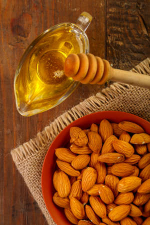 Almonds in a bowl on sacking next to honey with a spoon on a wooden table.の写真素材
