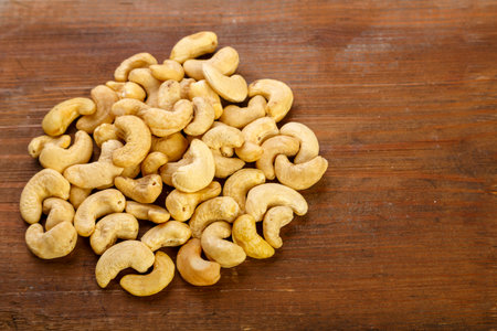 Cashew nuts are sprinkled on a dark wooden table.の写真素材