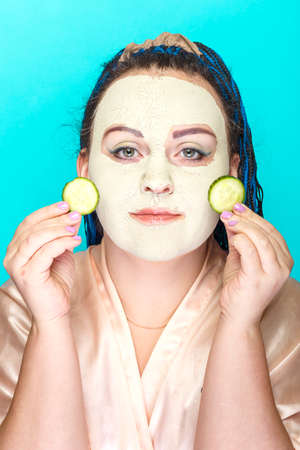 Woman with blue afro braids face in a frozen mask of green clay with pieces of cucumber in her hands.の写真素材