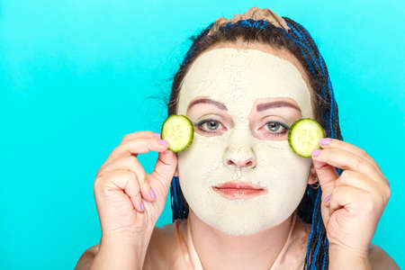 Jewish woman with blue Afro braids face in a frozen mask of green clay with pieces of cucumber in her hands.の写真素材