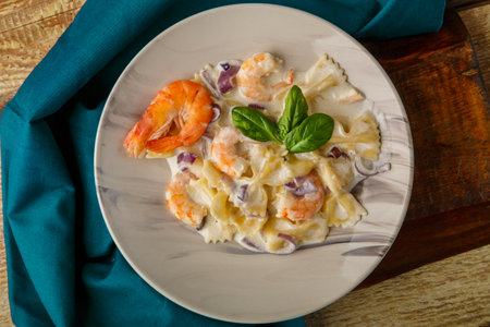 Farfalle pasta with shrimps in a creamy sauce on a gray plate on a wooden table on a blue napkin. Horizontal photoの写真素材