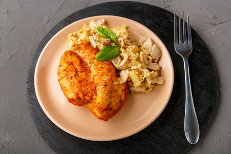 Baked chicken breast on a beige plate with pineapple salad on a table on a round stand on a concrete background next to a fork. Horizontal photoの写真素材