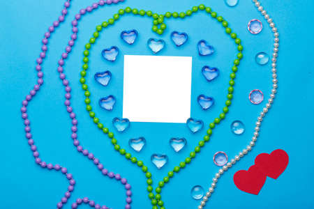 On a blue background, there is a heart of transparent pebbles in the shape of hearts in the middle of the postcard next to jewelry.の写真素材