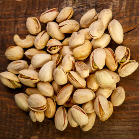 Pistachio nuts in shells scattering on a wooden table.の写真素材