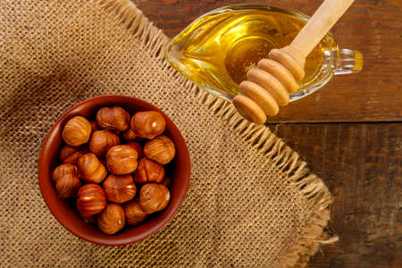 Hazelnuts in a bowl on a sacking next to honey with a spoon on a wooden table.の写真素材