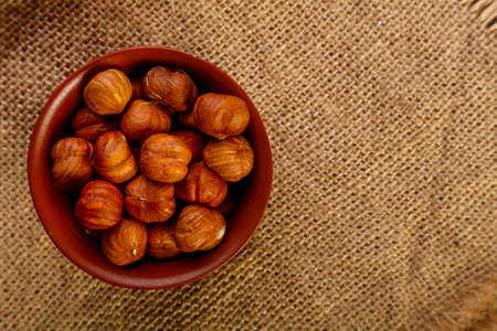 Hazelnuts in a clay cup on burlap on a wooden table.の写真素材