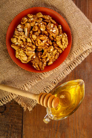 Walnuts in a clay bowl on burlap next to honey with a spoon on a wooden table.の写真素材