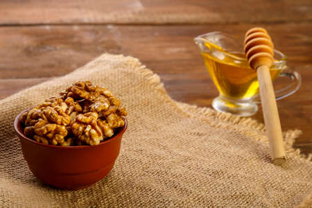 Walnuts in a clay bowl on a sacking next to honey with a spoon.の写真素材