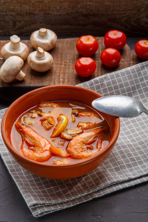 Tom yam soup with shrimps in a tureen on a concrete background next to a bowl with coconut milk tomatoes and mushroomsの写真素材