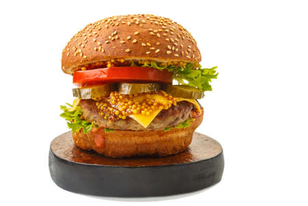 Classic burger with beef, cheese vegetables in sauce with mustard on a wooden round stand on a white background isolate.の写真素材