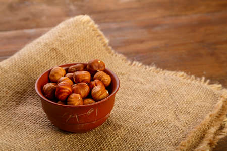 Hazelnuts in a clay cup on burlap on a wooden table.
