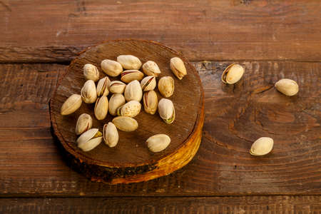 Pistachio nuts scattered on a round board on a wooden table.の写真素材