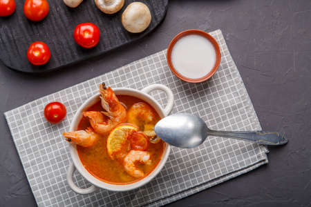 Tom yam soup with shrimps in a plate on the table on a napkin next to mushrooms and tomatoes.の写真素材