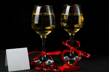Glasses with champagne tied with a red ribbon on a black background greeting card and a candlestick in the shape of a heartの写真素材