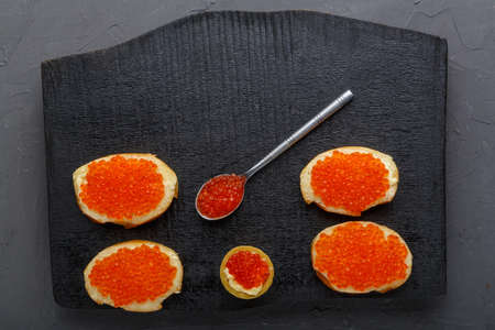 Canapes with butter and red caviar and a tartlet and a spoon with caviar on a black board on a concrete background.の写真素材