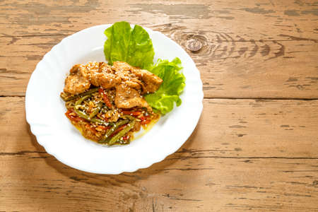 Vegetables with rice and chicken in a pan-Asian sauce with sesame seeds on green salad leaves on a wooden table in a plate.の写真素材