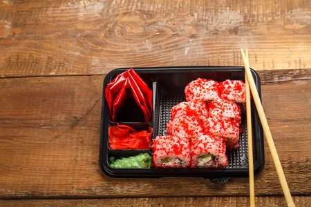 Roll with shrimp, cucumber, cream cheese and tobiko caviar and sticks in a box and soy sauce with ginger on a wooden background near the sticks. copy spaceの写真素材