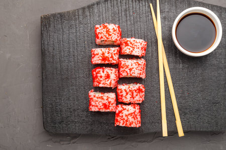 Roll with shrimp cucumber and tobiko caviar and sticks on a black carved board and soy sauce in a sauce bowl on a gray background.の写真素材