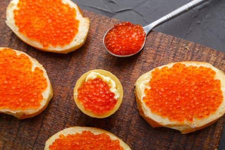 Bruschetta with butter and red caviar next to a spoon with caviar on a board on a concrete background.の写真素材