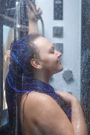 woman with blue afro hairstyle in the shower is washed with water.