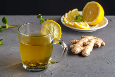 vitamin ginger drink with honey mint and lemon in a glass cup near ginger root and lemon on a concrete background.の写真素材