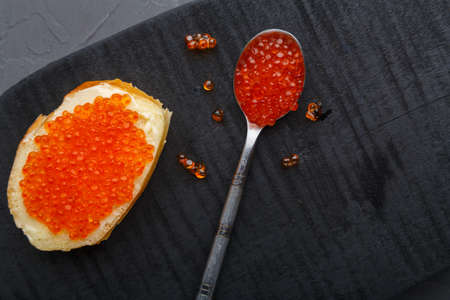 One toast with butter and red caviar near a spoon with caviar on a wooden board on a concrete background. Copy spaceの写真素材