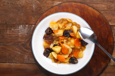A dish of Jewish cuisine tsimes with carrots and dates in a white plate on a round stand next to a spoon.の写真素材