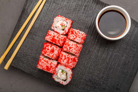 Roll with shrimp and tobiko caviar and sticks on a black board and soy sauce on a gray background. Copy spaceの写真素材