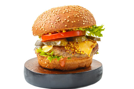 Classic burger with beef, cheese vegetables in sauce with French mustard on a bun with sesame seeds on a wooden round stand on a white background isolate.の写真素材