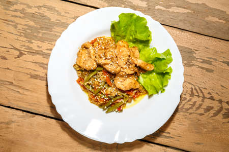 Vegetables with rice and chicken in a pan-Asian sauce with sesame seeds on green salad leaves on a wooden table in a plate.の写真素材