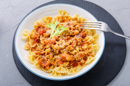 Pasta in tomato bolognese sauce on a round black stand on a concrete background near a fork and ripe tomatoの写真素材