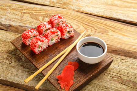 Roll with shrimp cucumber and tobiko caviar and sticks on a board and soy sauce in a sauce bowl on a wooden background.の写真素材