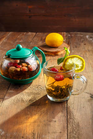 green tea in a glass cup with strawberries mint and lemon on a wooden table next to a teapot.の写真素材