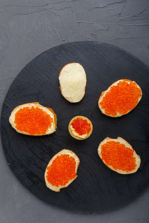 Canapes with butter and red caviar on a black round board on a concrete background copy spaceの写真素材